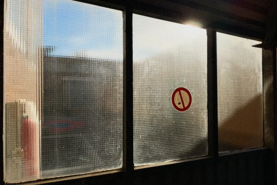Ein Blick durch strukturierte Glasfenster zeigt eine Außenansicht mit einem runden Warnzeichen.